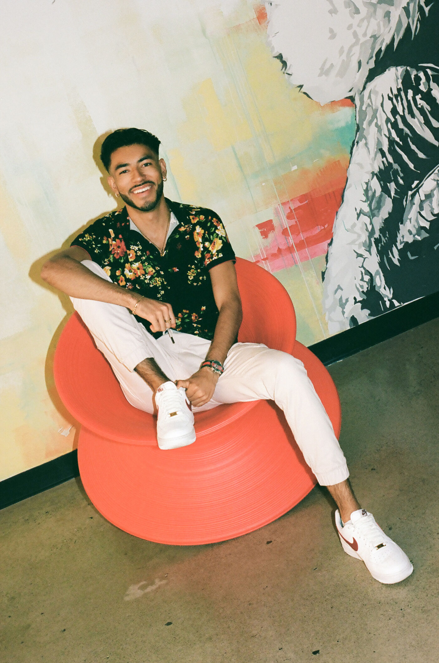 A man with a beaming smile relaxes in a modern red chair.